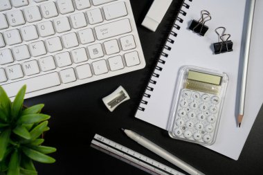 Bilgisayar klavyesi, iş gereçleri, bitki ve kopya alanı olan siyah beyaz ofis masası. Çalışma masası ile üst görünüm ve metin için yer kopyala.