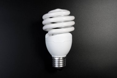 Karanlık odada enerji tasarrufu kavramı için siyah zemin üzerinde bir floresan ampul. Düşünmek için enerji tasarrufu ampulü.