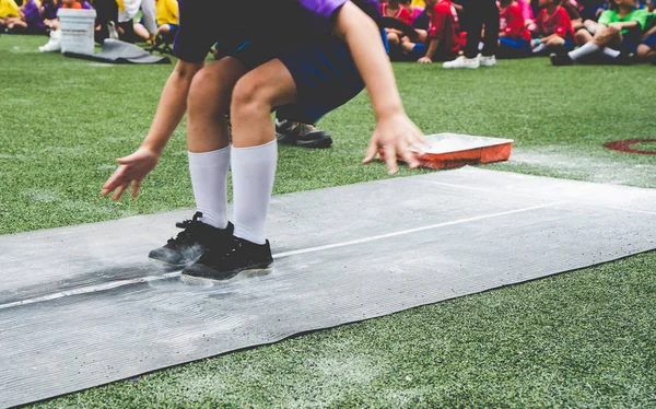 Students boy taking long jump on rubber board pid or sand pid during a school sport competition day. School sports day long jump competition (Focus on foots).