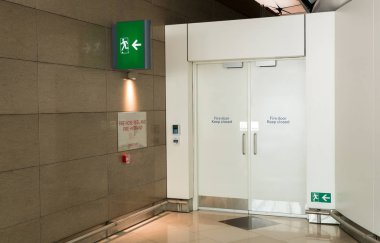 Havaalanı terminalinin acil çıkış yolundaki yangın çıkışı ve yangın çıkışı ışık kutusu. Acil durum işaretine karşı yeşil acil çıkış kapısı yönü.