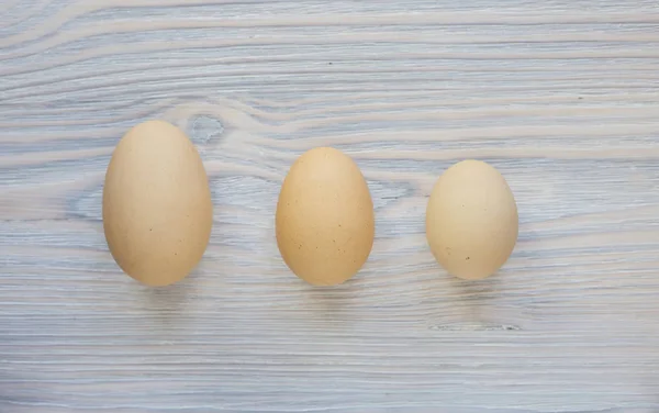 Three different size eggs on the light wood background tell us t — Stock Photo, Image