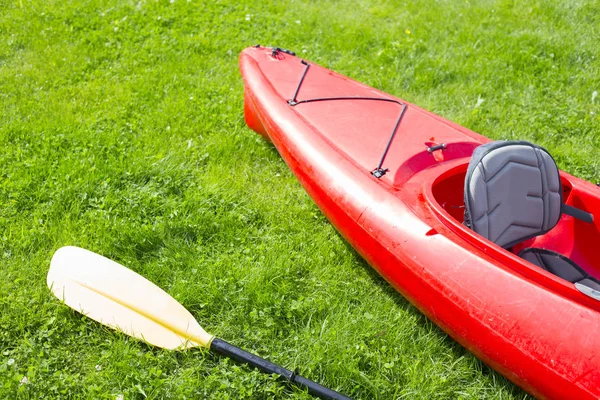Red kayak and yellow row lays on the green grass and waiting for — Stock Photo, Image