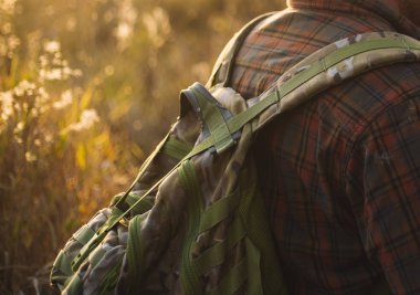 Kareli gömlekli, sırt çantalı, güneş ışığında insanlar. Tarlalarda saklanan ve barış için dua eden bir asker ya da çimenlerde yürüyüp avını arayan bir avcı olabilir.