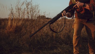 Hunter 'ın elleri silah tutuyor. Dışarıda dikilen ve kareli gömlek, deve pantolonu, deri cephane kemeri ve akıllı saat giyen bir adam. Seçici odaklı fotoğraf