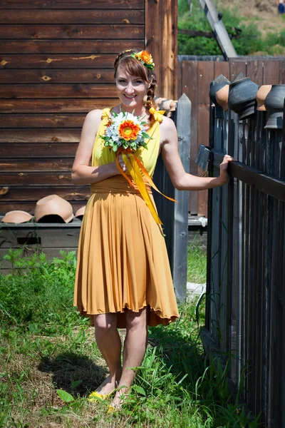 Νύφη νεαρή όμορφη κοπέλα σε ένα λαμπερό πορτοκαλί φόρεμα στο ρωσικό ξύλινο σπίτι. Καλοκαίρι μπουκέτο στα χέρια της νύφης. Διακόσμηση από λουλούδια στο χτένισμα τα μαλλιά τους. Νύφη hippie. Ηλιόλουστη διάθεση. — Φωτογραφία Αρχείου