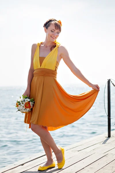 Junge schöne Mädchen in der leuchtend orangefarbenen Braut auf einem Hintergrund des Sees. Sommerstrauß in Händen der . — Stockfoto