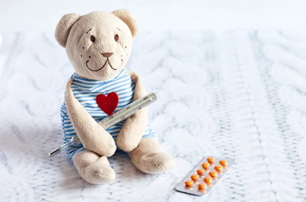 Urso de pelúcia de brinquedo macio de crianças com pílulas leva a temperatura de um termômetro de vidro de mercúrio. doença infantil . — Fotografia de Stock
