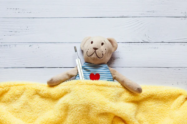 Enfants peluche peluche ours au lit avec thermomètre et pilules, prendre la température d'un verre de mercure. Sur fond de bois blanc. Je joue à l'hôpital. maladie infantile . — Photo