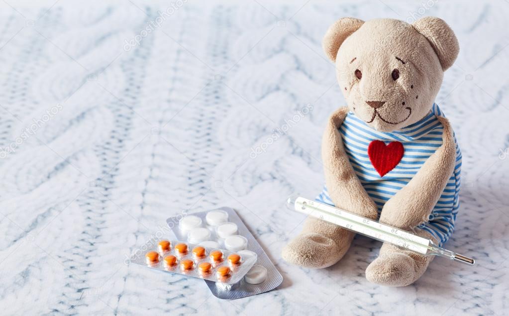 childrens soft toy teddy bear with pills takes the temperature of a mercury glass thermometer. childs disease.