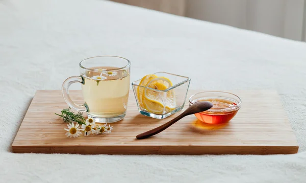 Té de hierbas en taza de vidrio con flores de manzanilla, cúrcuma y miel en una tabla de madera. Tratamiento de la bebida caliente. Tratamiento de remedios caseros en la cama . — Foto de Stock