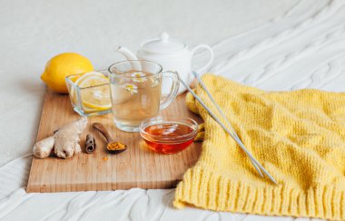 Bitkisel çay papatya çiçeği, zerdeçal ve ballı bir ahşap tahta üzerinde. Zencefil ile sıcak içecek tedavisinde. Yatakta halk ilaçları tedavisinde. Örgü iğne ve iplik örme için.