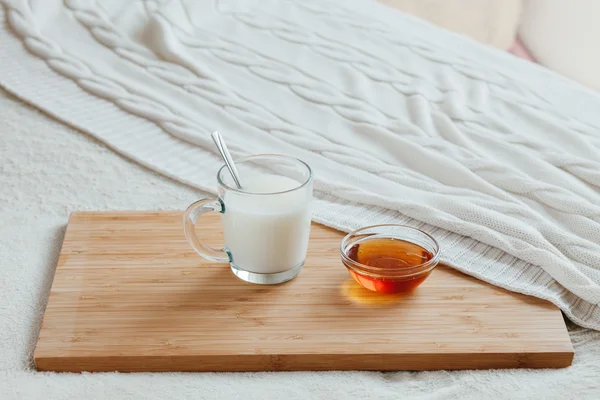 Leche caliente en una taza de vidrio y miel en una tabla de madera. Tratamiento de la bebida caliente. Tratamiento de remedios caseros en la cama . — Foto de Stock