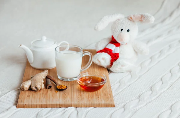 Горячее молоко в стакане и мед на деревянной доске. Лечение детей горячим напитком. Лечение народных лекарств в постели. Мягкий игрушечный кролик для вашего ребенка . — стоковое фото