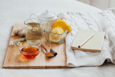 Bitkisel çay papatya çiçeği, zerdeçal ve ballı bir ahşap tahta üzerinde. Zencefil ile sıcak içecek tedavisinde. Yatakta halk ilaçları tedavisinde. Eğlenceyle ilgili bir kitap.