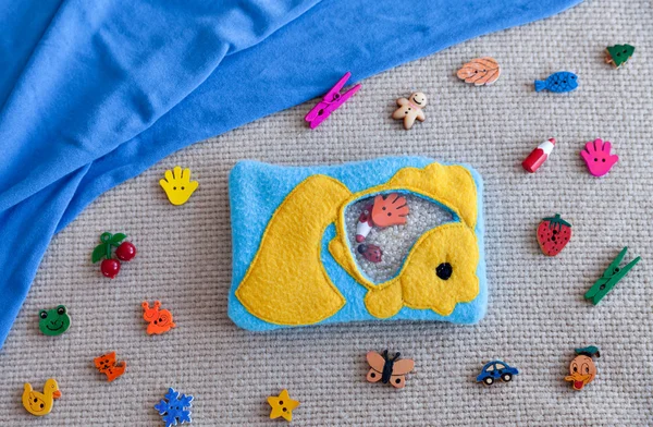 Childrens toy goldfish made of colored fleece for motor development. Bag fleece filled with plastic beads and figurines on the background of scattered toys and blue fabric. handmade toys.