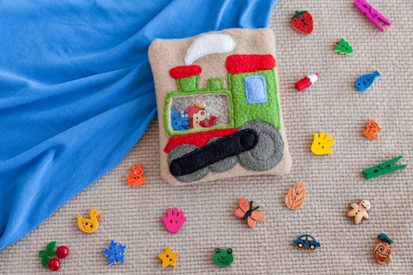 Locomotiva de brinquedo macio infantil feita de velo colorido para desenvolvimento motor. Mala de lã cheia de contas de plástico e estatuetas no fundo de brinquedos espalhados e tecido azul. brinquedos artesanais . — Fotografia de Stock