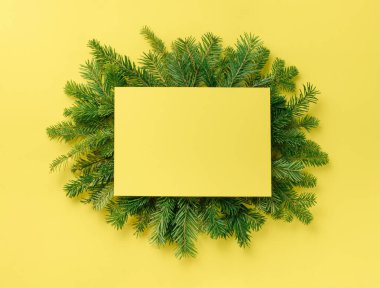 Noel kompozisyonu. Noel süslemeleri, sarı arka plandaki köknar dalına boş kağıt. Düz konum, üst görünüm, kopyalama alanı.