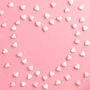 Sevgililer Günü için 14 Şubat 'ta kompozisyon. Hassas pembe arka plan, sarı ve pembe şekerlemeler kalp şeklinde serilmiş. Tebrik kartı. Düz konum, üst görünüm, kopyalama alanı.