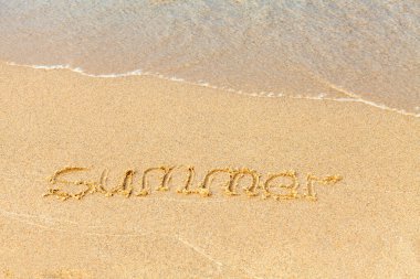 Güneşli bir sahilde mesaj. Yaz kelimesi el yazısıyla kumla yazılır ve bir deniz dalgası tarafından sürüklenir. Kumsalda tatil kavramı. Boşluğu kopyala.