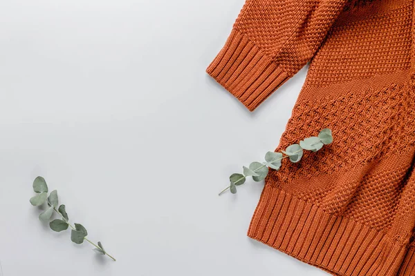 Зимняя композиция. Оранжевый свитер и ветвь эвкалипта на белом фоне. Осень, зимняя концепция. Плоская кладка, вид сверху, копировальное пространство — стоковое фото