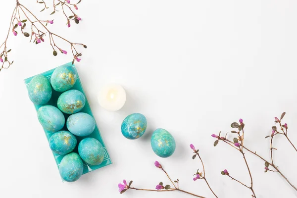 Bonne carte de Pâques. Composition minimaliste élégante de turquoise avec des œufs de Pâques en or sur fond blanc. Bougies et fleurs printanières délicates. Pose plate, vue du dessus, espace de copie . Photo De Stock