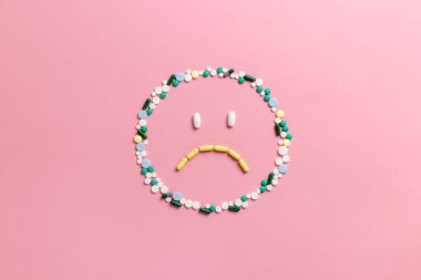 Emoji şeklinde pembe bir arka planda hapların ve kapsüllerin bileşimi. Üzücü duygular. Psikolojik yardım. Uzayı kopyala Yukarıdan bak. Düz yatıyordu.