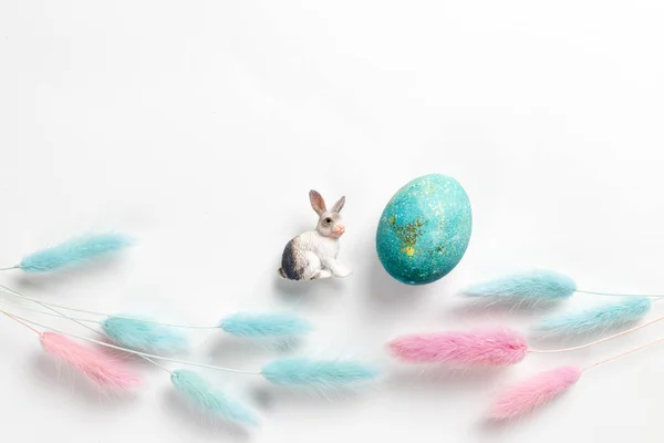Bonne carte de Pâques. Composition minimaliste élégante de turquoise avec des œufs de Pâques en or sur fond blanc. Figurine de lapin et délicates fleurs printanières. Pose plate, vue du dessus, espace de copie . Image En Vente