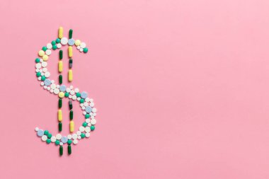 The concept of the cost of drugs and drug trafficking. Composition of pills and capsules on a pink background in the form of a dollar sign. Copy space. View from above. Flat lay.