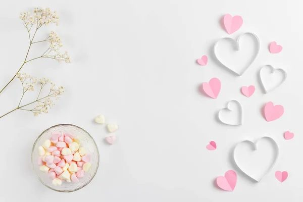 Komposition für den Valentinstag am 14. Februar. Zarte Komposition aus rosa Herzen aus Papier und herzförmigen Marshmallows auf weißem Hintergrund. Grußkarte. flache Lage, Draufsicht, Kopierraum. Stockfoto