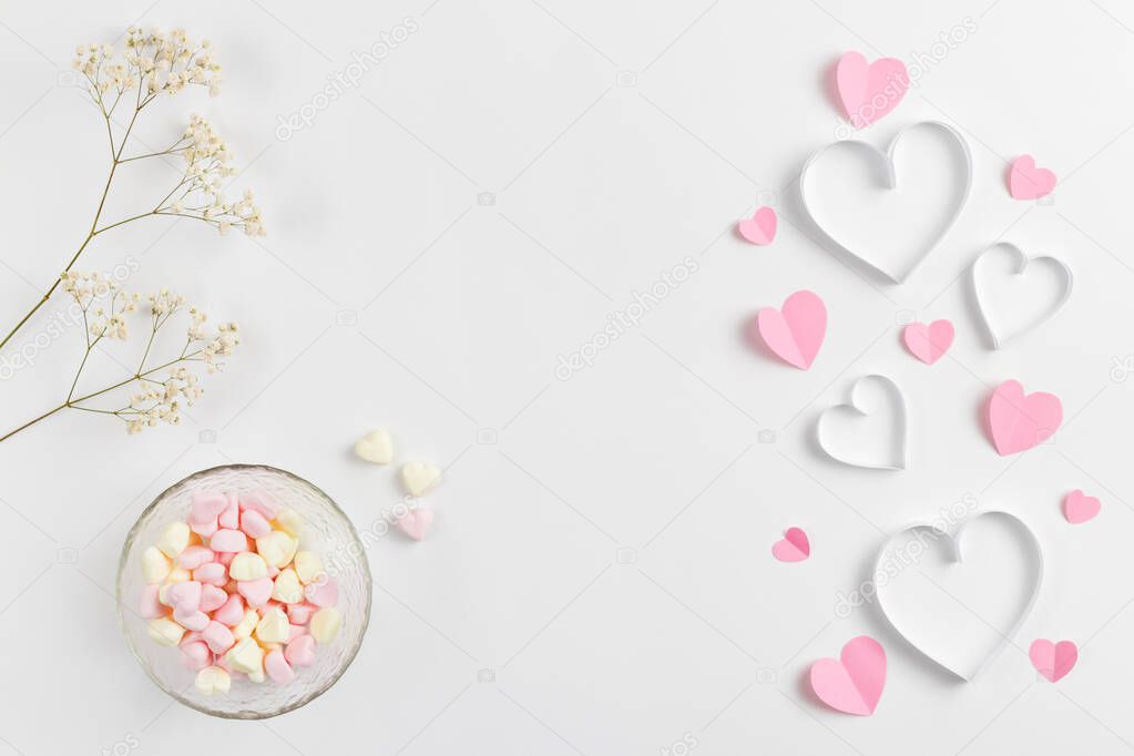 Composition for Valentines Day February 14th. Delicate composition of pink hearts made of paper and heart-shaped marshmallows on a white background. Greeting card. Flat lay, top view, copy space.