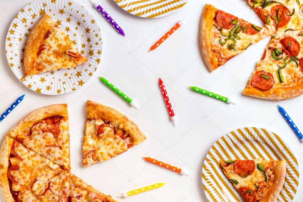 Pieces of pizza and colored candles for a cake on a white background. Birthday with junk food. Childrens party. Top view with copy space for text. Flat lay