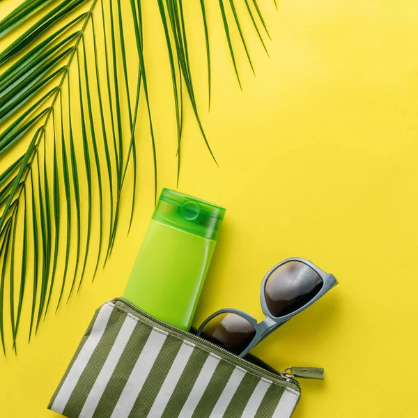 Summer background. Composition striped beach cosmetic bag with sunblock and sunglasses on a yellow background. Summer vacation concept, sunscreen cosmetics and accessories. Top view. Copy space. 스톡 이미지