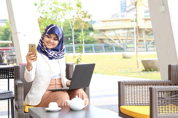 Азиатская мусульманка головной платок сидя открытый компьютер смартфон — стоковое фото