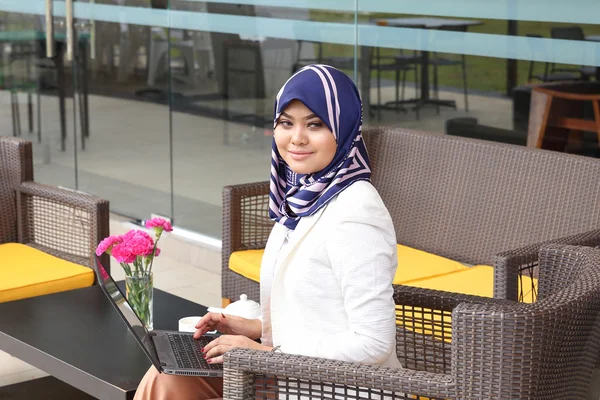 Азиатская мусульманка головной платок сидя открытый ноутбук улыбка смотреть — стоковое фото