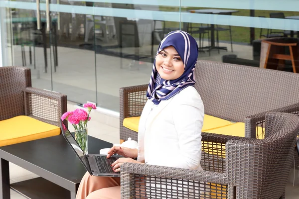 Азиатская мусульманка головной платок сидя открытый ноутбук улыбка смотреть — стоковое фото