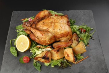 Kızarmış tavuk kanatlı tavuk ve fırında patates salatalı limon siyah tahta kesme tahtası siyah arka planda.