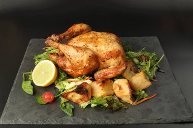 Kızarmış tavuk kanatlı tavuk ve fırında patates salatalı limon siyah tahta kesme tahtası siyah arka planda.