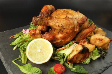 Kızarmış tavuk kanatlı tavuk ve fırında patates salatalı limon siyah tahta kesme tahtası siyah arka planda.