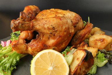 Kızarmış tavuk kanatlı tavuk ve fırında patates salatalı limon siyah tahta kesme tahtası siyah arka planda.