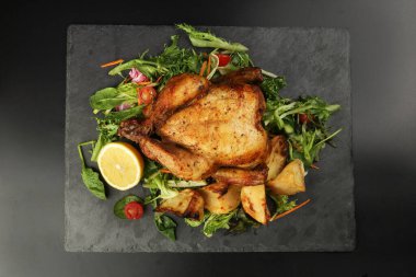 Kızarmış tavuk kanatlı tavuk ve fırında patates salatalı limon siyah tahta kesme tahtası siyah arka planda.