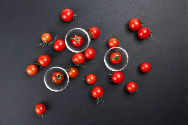 Red ripe cherry tomato with stem on black paper background copy text space mini glass bowl