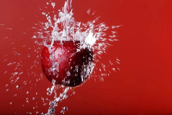 red apple under a waterfall splashing on a red background