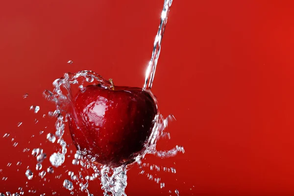 Red apple under a waterfall splashing on a red background — Stock Photo, Image