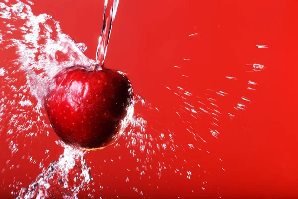 Red apple under a waterfall splashing on a red background — Stock Photo, Image
