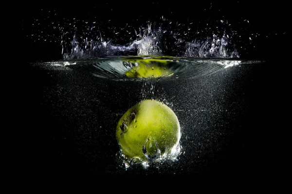 Green apple falling in water with splash on black background.