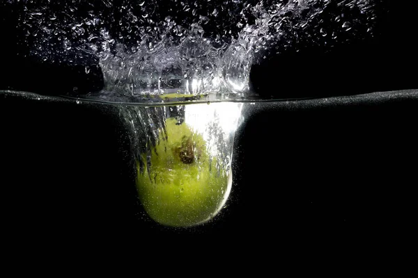 Green apple falling in water with splash on black background