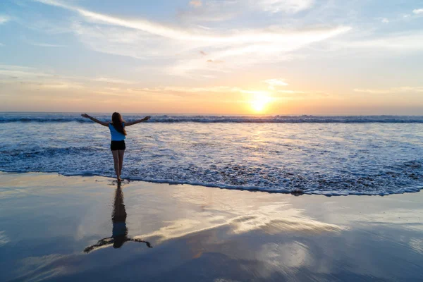 Mulher braços abertos sob o pôr do sol no mar com uma silhueta re — Fotografia de Stock