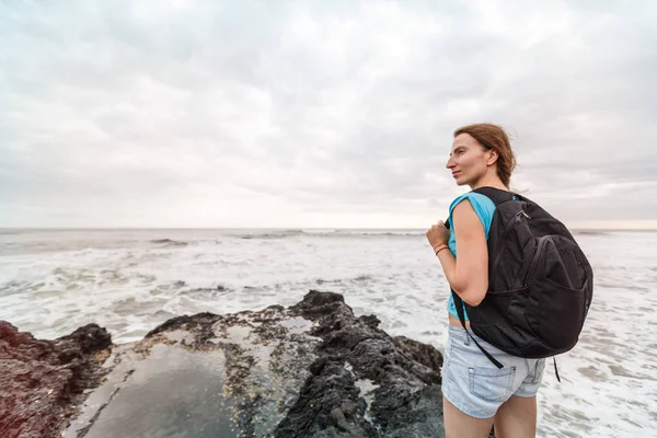 Girl with backpack coastline. Traveler female on background beach seascape.