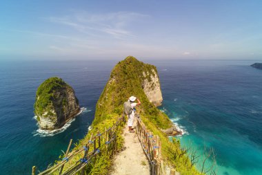 Mens backpack standing on Kelingking beach cliff on Nusa Penida island clipart