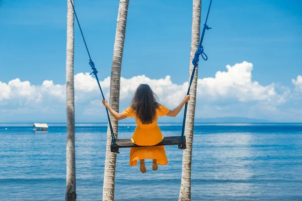 Conceito de férias. Jovem feliz em vestido amarelo sentado no balanço apreciando vista mar . — Fotografia de Stock